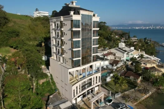 Imagem de um edifício residencial moderno localizado na orla de uma cidade à beira-mar, com vista para o mar e bairro residencial ao redor, na cidade de Itapema